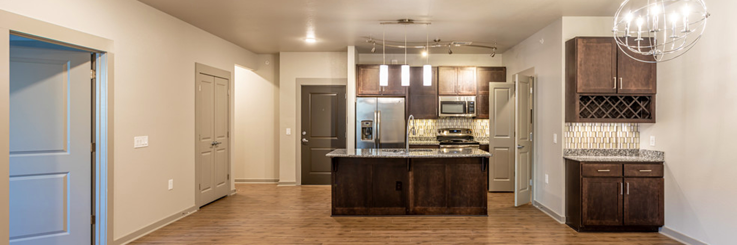 Photo of an empty apartment at Bowman Pointe in Little Rock, Arkansas. It shows a view of the island kitchen, built-in wine rack and dry bar, and dining nook.